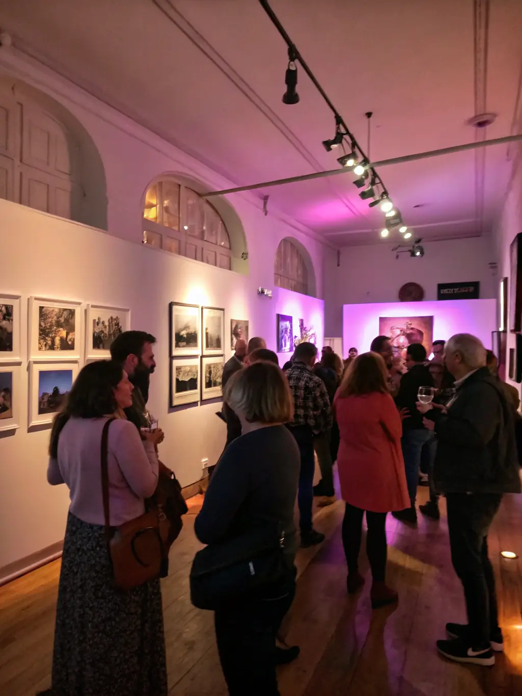 A vibrant photograph capturing the opening night of a COULEURS EN PARTAGE exhibition, featuring attendees admiring a colorful abstract painting, with Ivy Langue giving a speech in the background.